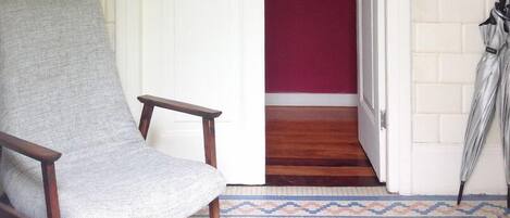 A chair with a grey fabric, a wooden floor, a red wall, and a patterned rug.