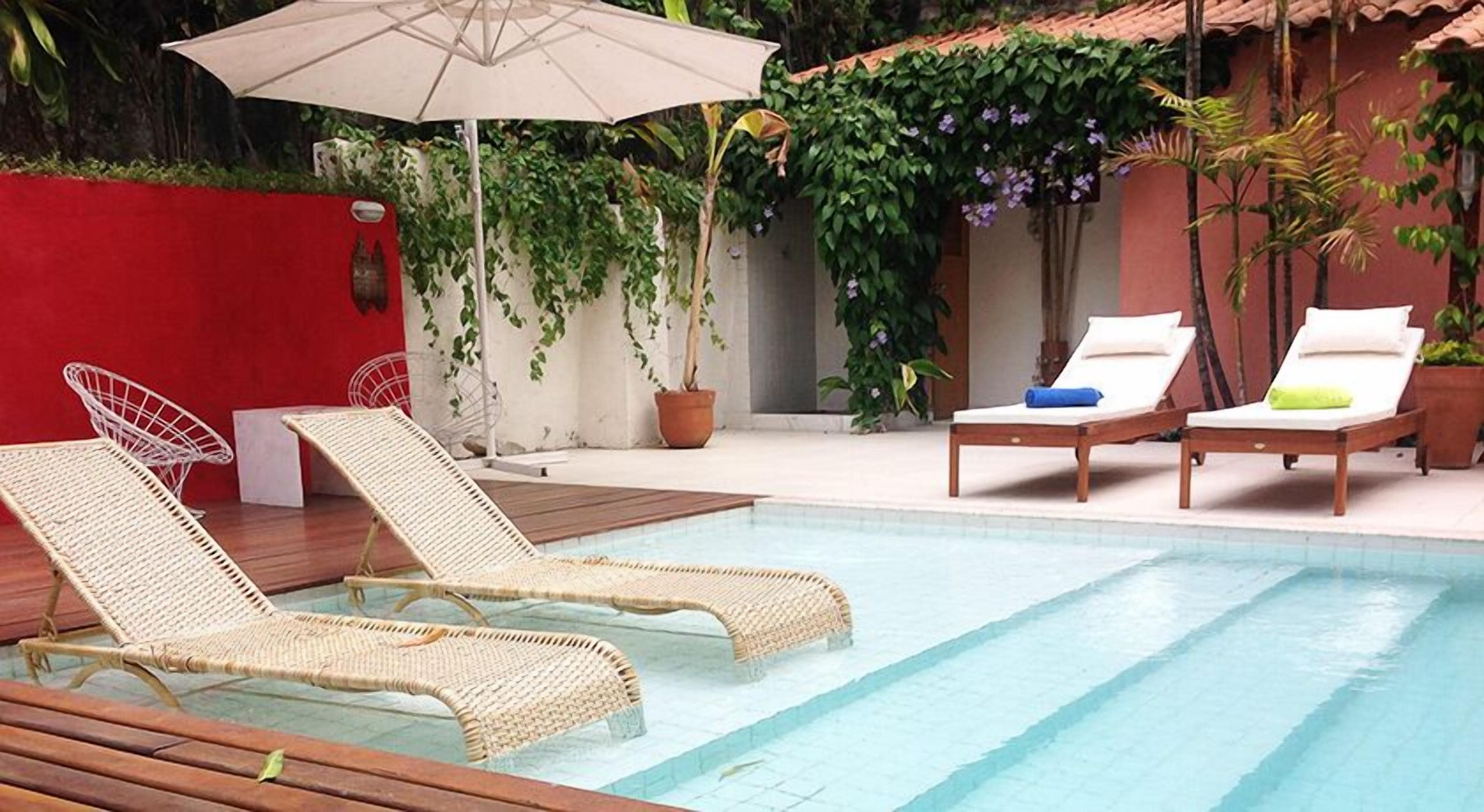 A pool area with two lounge chairs, a red wall, and potted plants.