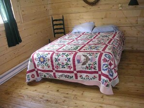 Een kamer met houten lambrisering en een bed met een quilt met bloemenmotief.