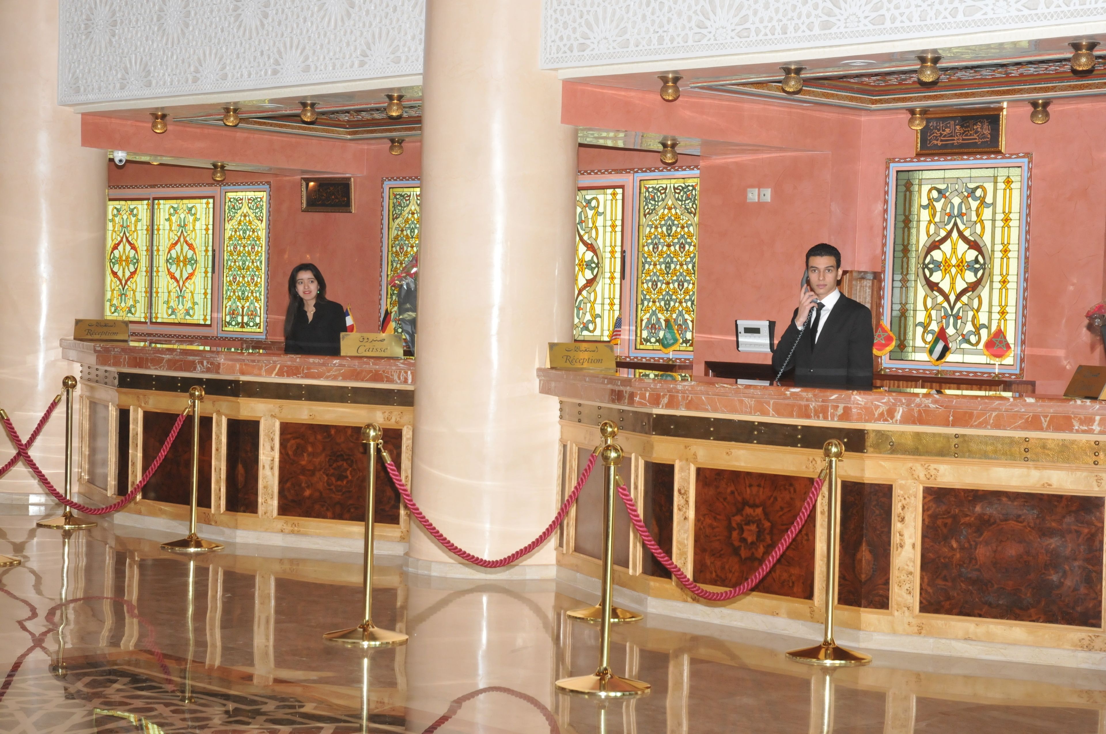 A reception area with a marble counter, glass doors with intricate designs, and a red rope barrier.