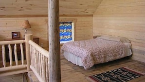 Un dormitorio tipo cabaña de madera con cama, ventana con vistas y baranda de madera.