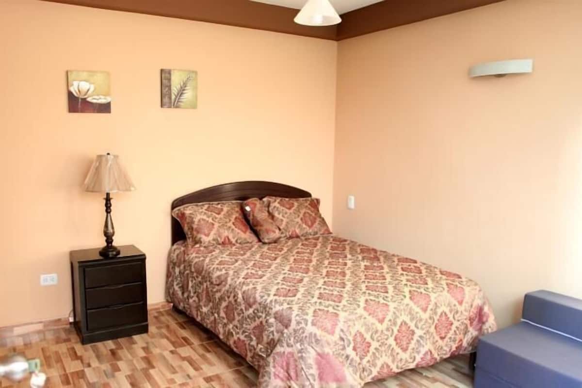 A bedroom with a bed, a nightstand, a lamp, and two wall art pieces.