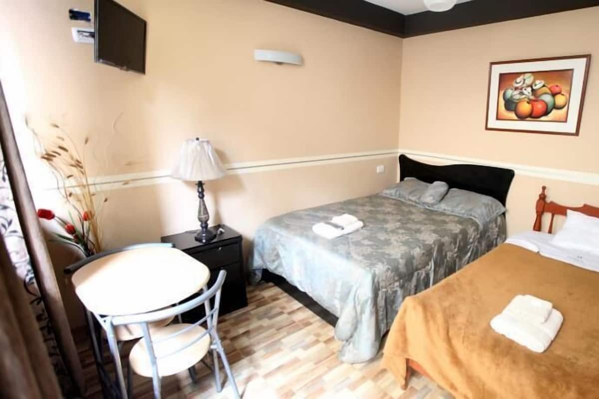 A hotel room with two beds, a small table, a chair, a lamp, and a painting on the wall.