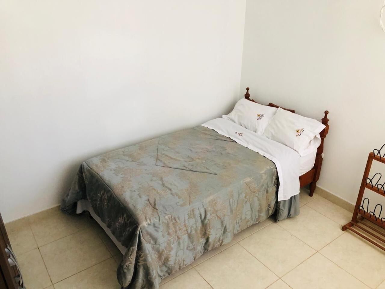 A single bed with a floral bedspread and white pillows, a wooden headboard, and a metal rack on the right side.