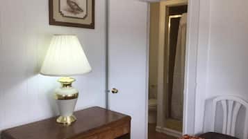 Une pièce avec un bureau en bois, une lampe, un tableau encadré au mur et une porte donnant sur une salle de bain.