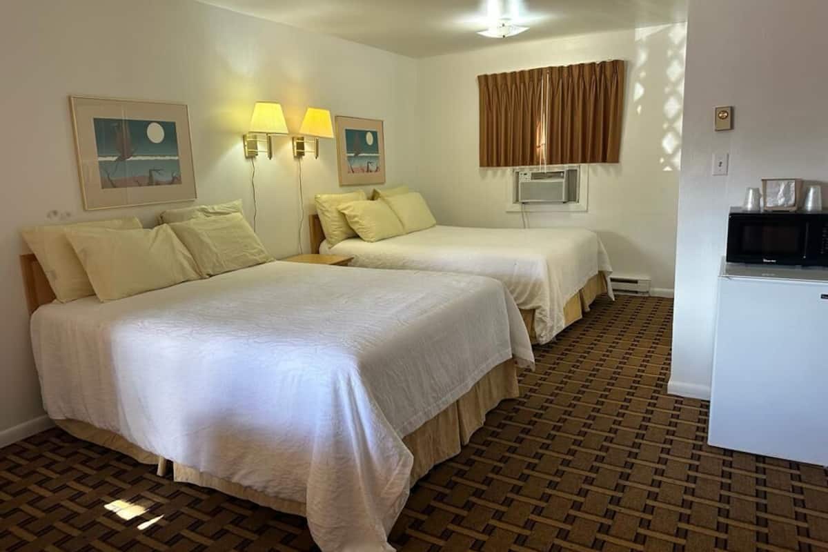 A hotel room with two beds, a desk with a microwave, and a window with curtains.