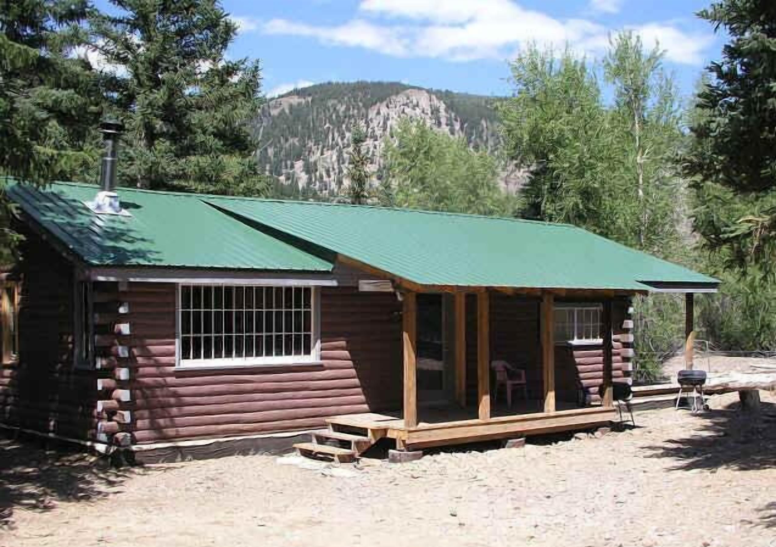 A log cabin with a green roof, a porch, and a window with bars.