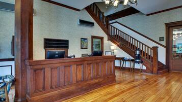 A reception desk with a wooden finish, a staircase with wooden railings, and a chandelier.
