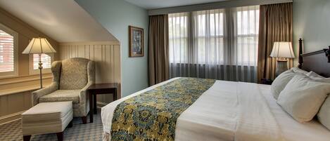 Habitación de hotel con una cama grande, una silla, una mesita y una ventana con cortinas.