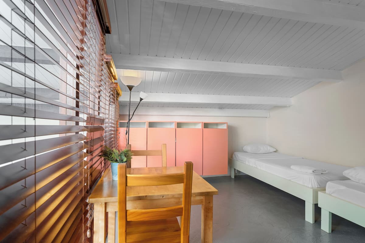 A room with a wooden table, a bench, a bed, and a pink wardrobe.