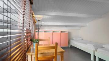 Ein Zimmer mit einem Holztisch, einer Bank, einem Bett und einem rosa Kleiderschrank.