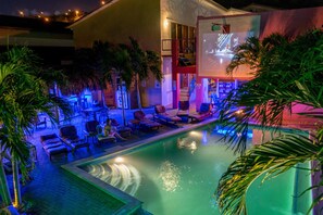 Zona de piscina con sillones de descanso y palmeras, una escalera y un edificio con balcón.
