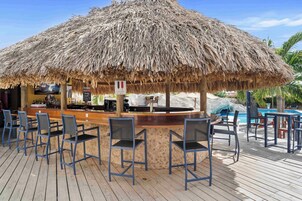 Uma área de bar com telhado de palha, deck de madeira e banquetas.