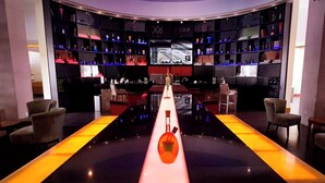 Un bar moderno con mostrador central, estanterías llenas de botellas y asientos a ambos lados.