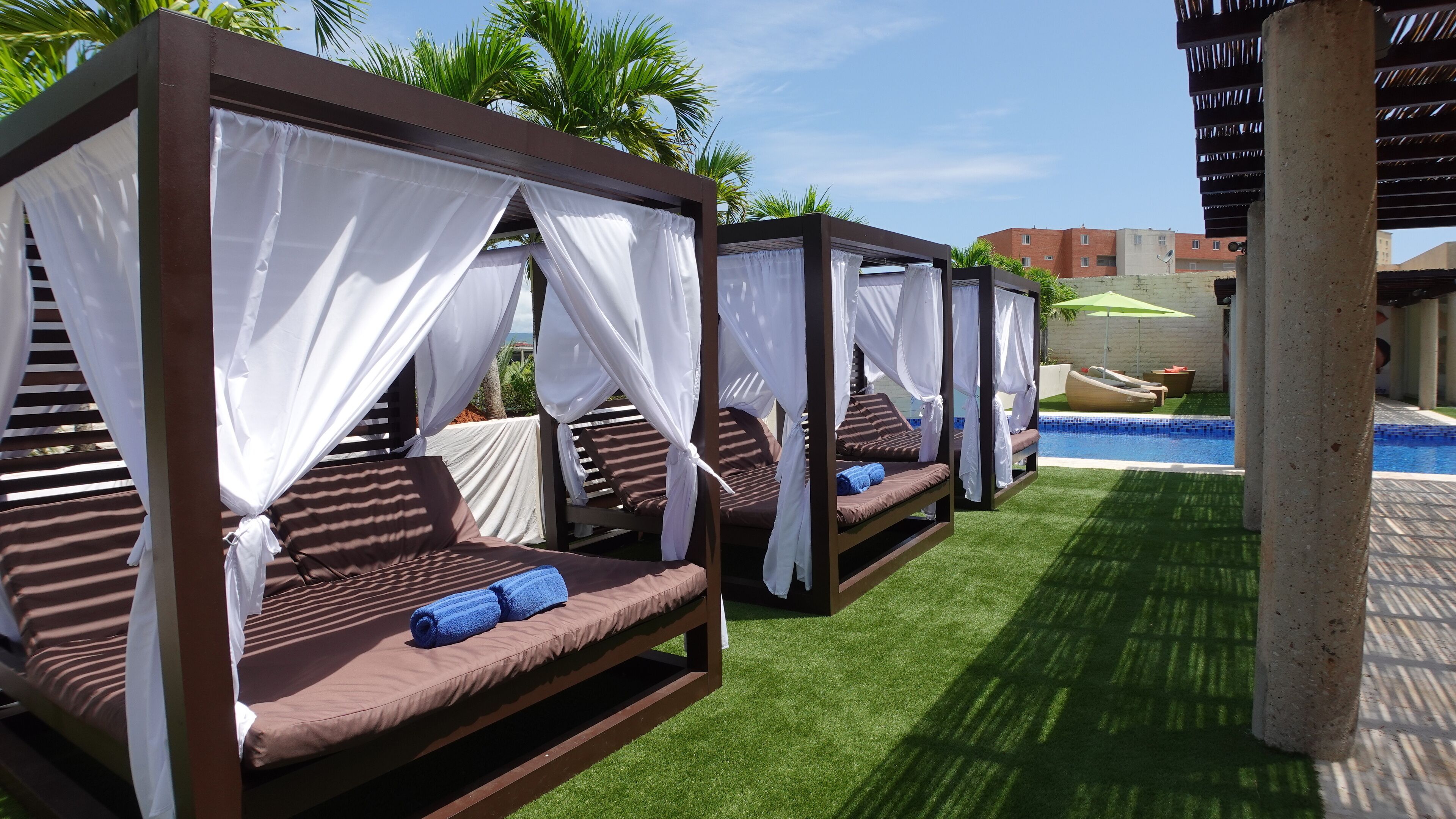 A poolside area with four canopy beds, each with a pillow and a towel.