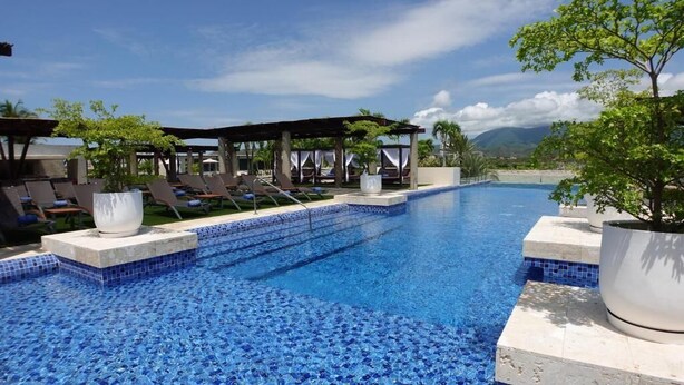 Zona de piscina con sillones de descanso y una pérgola, rodeada de vegetación y montañas al fondo.