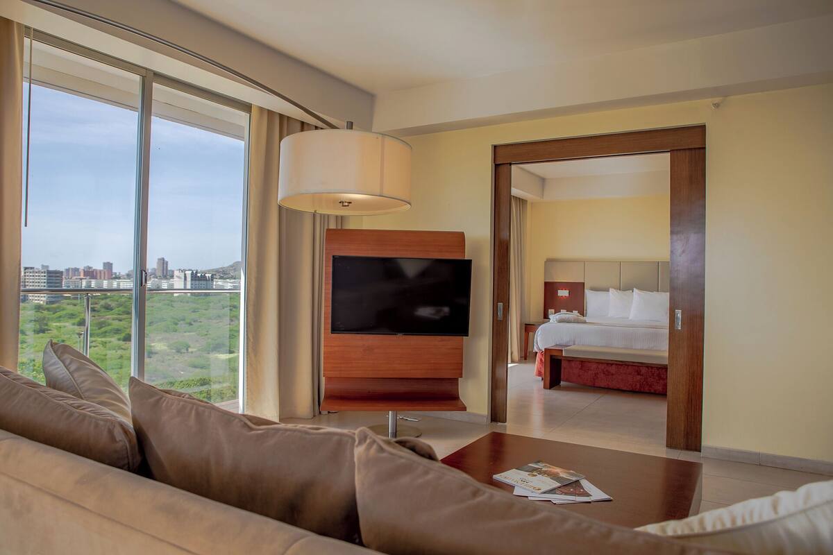 Une chambre d’hôtel moderne dotée d’une grande fenêtre, d’un téléviseur à écran plat, d’un canapé confortable et d’un lit parfaitement fait.