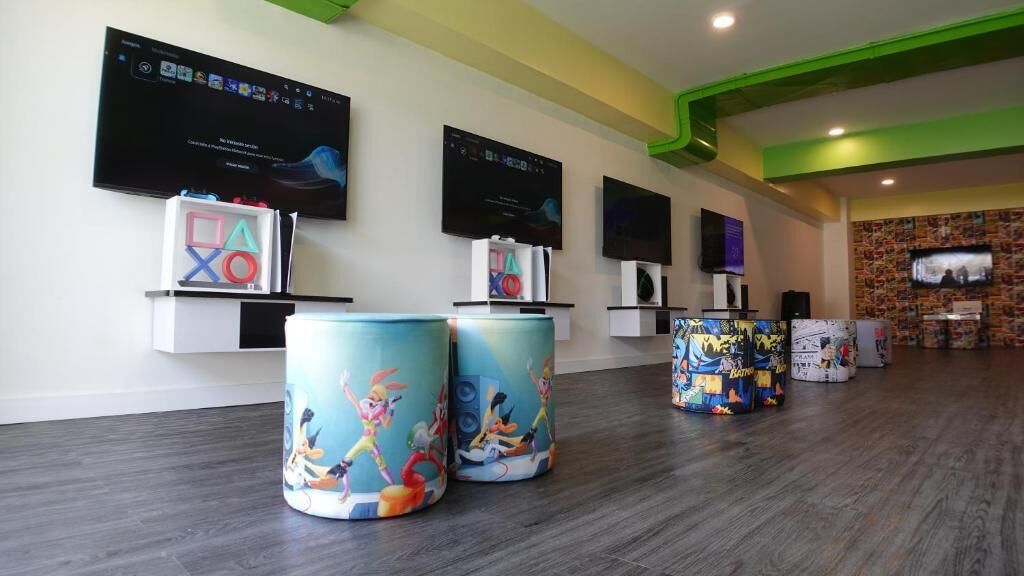 A modern lobby with a wooden floor, multiple TVs on the wall, and colorful cylindrical decorations.
