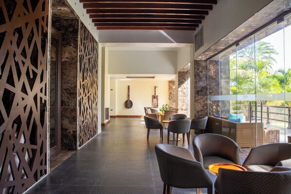 Een moderne hotel lobby met een lange gang, een eetgedeelte met stoelen en een tafel, en een groot raam met uitzicht op groen.