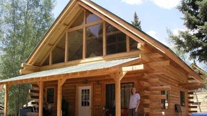 Une cabane en rondins dotée d’une grande véranda, d’un porche abrité et d’un garage visible.