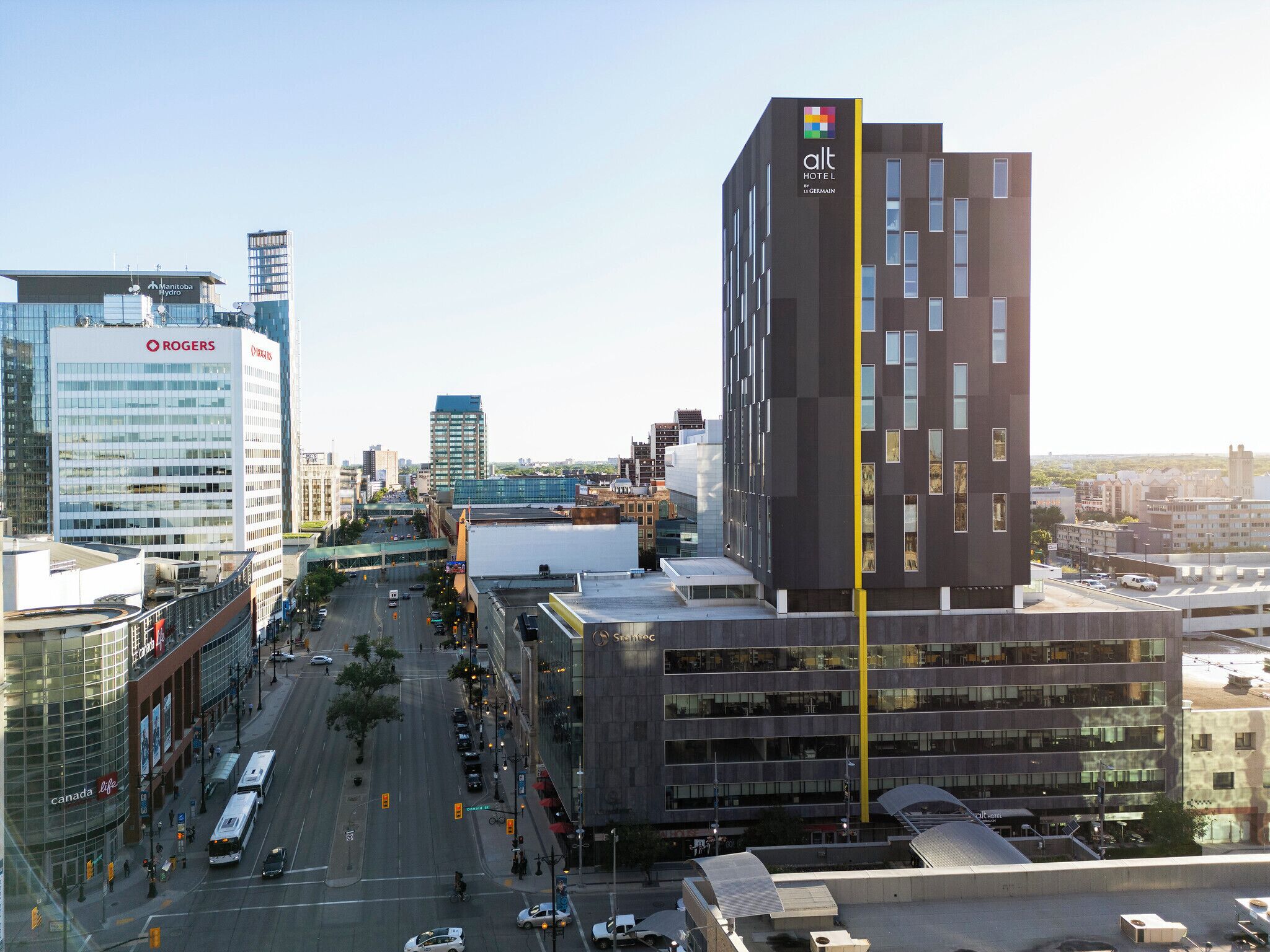 Un hotel moderno con una llamativa banda vertical amarilla, rodeado de edificios urbanos y una calle concurrida.