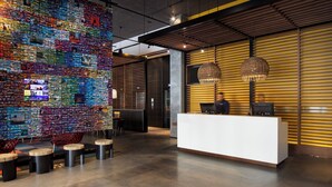 A modern reception area with a colorful mosaic wall, a white reception desk, and a seating area with stools. - Alt Hotel Winnipeg (Winnipeg)