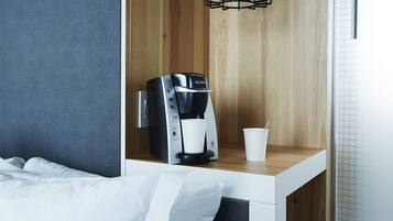 A modern hotel room with a bed, a wooden nightstand, a Keurig coffee maker, and a cup of coffee.
