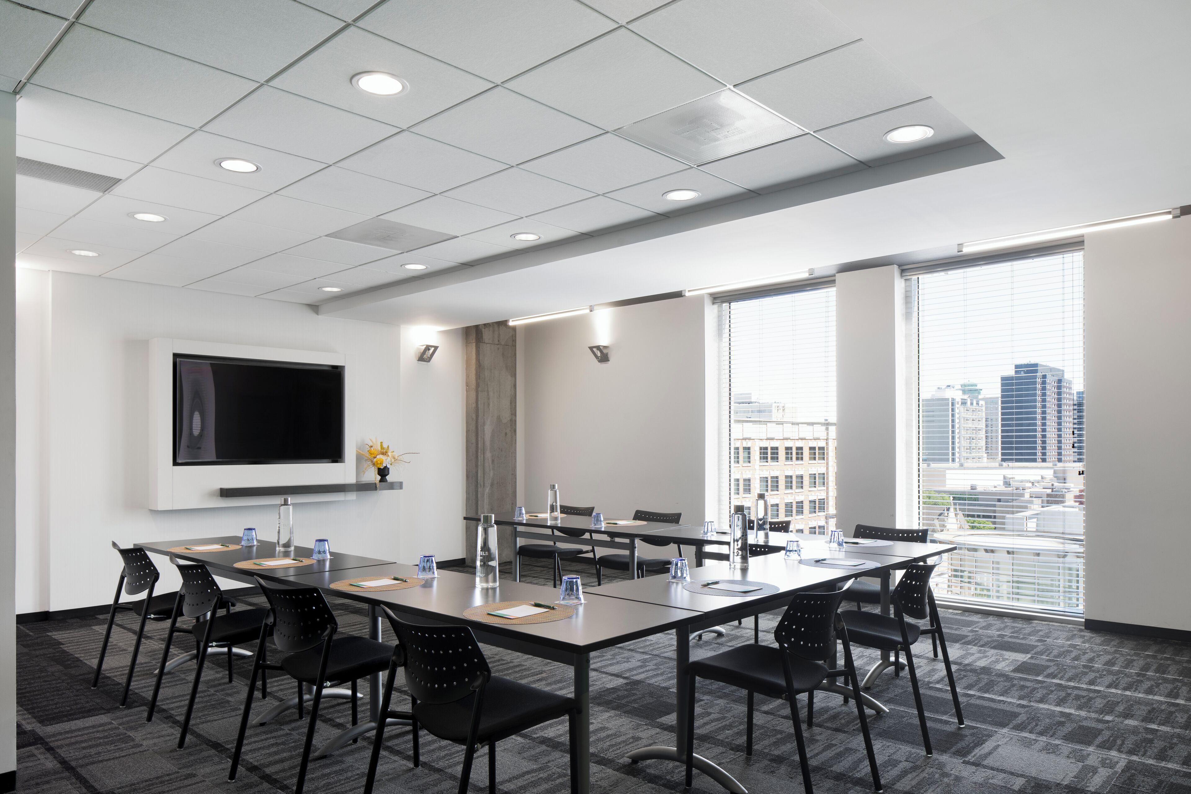 A conference room with a large table, chairs, a flat-screen TV, and a city view through large windows.