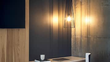 A modern dining area with a wooden panel wall, a concrete accent wall, a hanging light fixture, a table with a chair, and a bench.