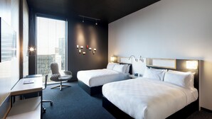 A hotel room with two beds, a desk, a chair, and a large window with blinds. - Alt Hotel Winnipeg (Winnipeg)