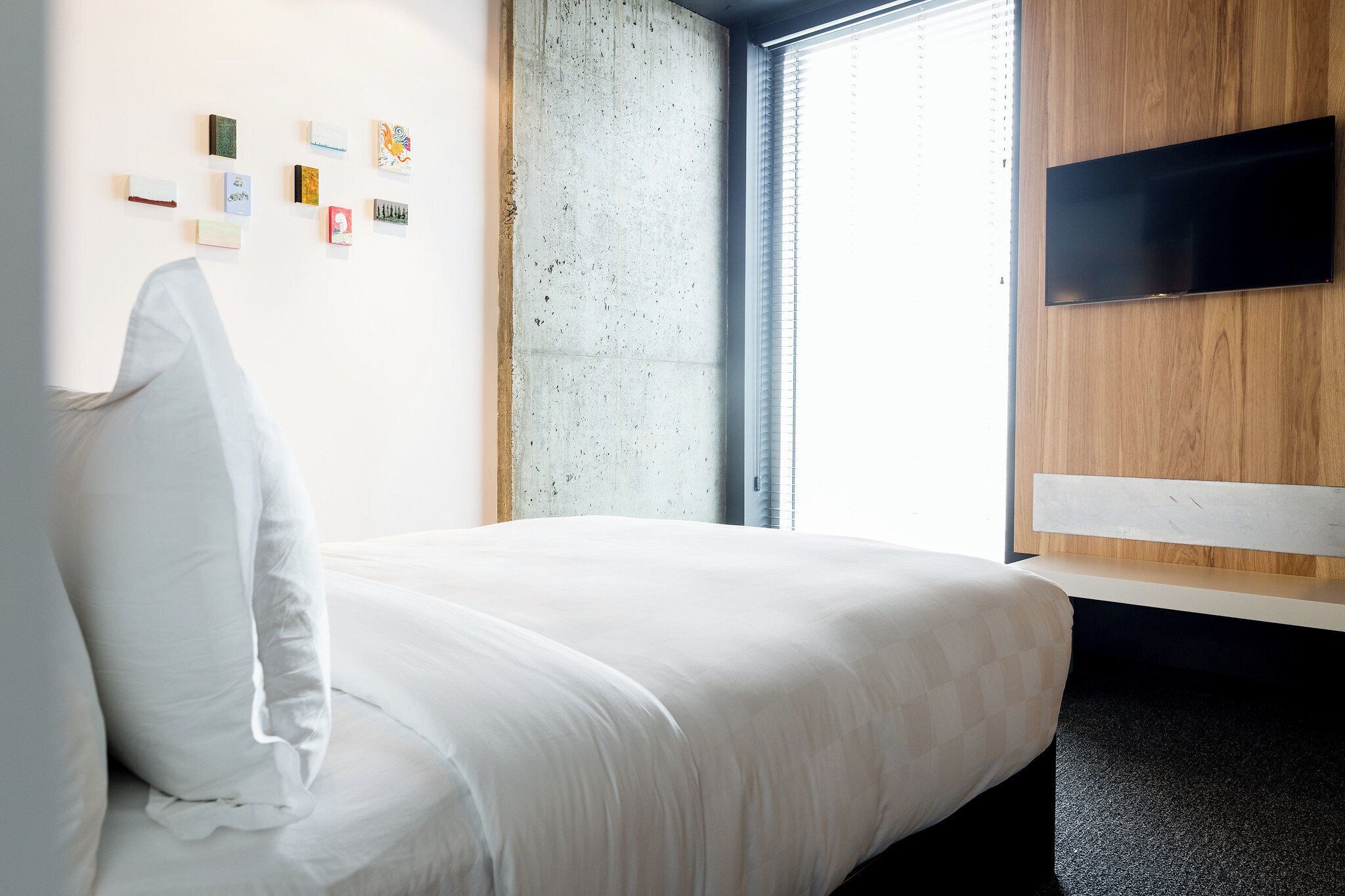 Quarto de hotel com uma cama, televisão fixada na parede e janela com persianas.