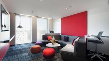 Un salón moderno con un sofá gris, otomanas rojas y una mesa de centro blanca. Hay una pared de acento roja y una ventana con persianas.
