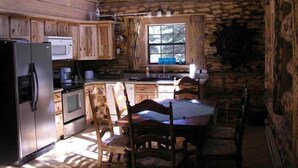 A rustic cabin-style kitchen with wooden cabinets, a refrigerator, stove, and a dining table with chairs.