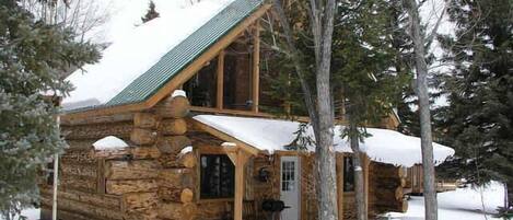 A log cabin with a two-story structure, a porch, and a snow-covered roof.
