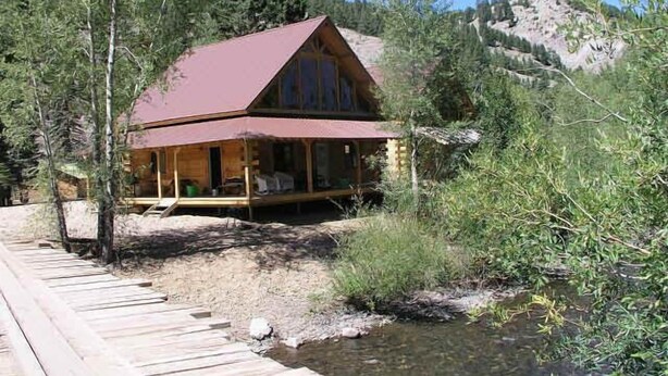A cabin with a red roof, wooden deck, and a small stream in front. - Silver Queen Vacation Rental (Lake City)