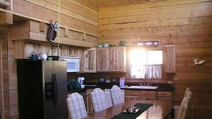 A wooden cabin interior with a dining table, chairs, a refrigerator, a microwave, and a window with curtains. - Silver Queen Vacation Rental (Lake City)