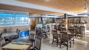 A restaurant with multiple tables and chairs, a bar area, and cityscape views through large windows. - Hotel Colon (Benidorm)