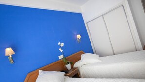 A hotel room with two beds, a wooden headboard, a nightstand with a lamp, and a wall-mounted light fixture. - Hotel Colon (Benidorm)