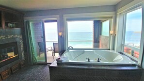 A bathroom with a large bathtub, a fireplace, and a view of the ocean.