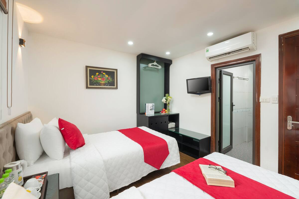 A hotel room with two beds, a TV, an air conditioner, a mirror, and a shower area.