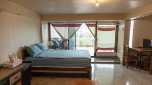 A bedroom with a bed, a desk, and a chair. There is a balcony with a view of the outside. - INA House (Chiang Mai)