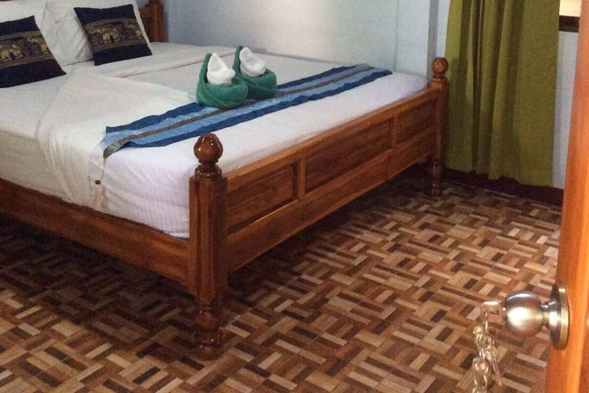 Une pièce avec un lit en bois, un parquet à motifs, un rideau vert et un ventilateur de plafond.