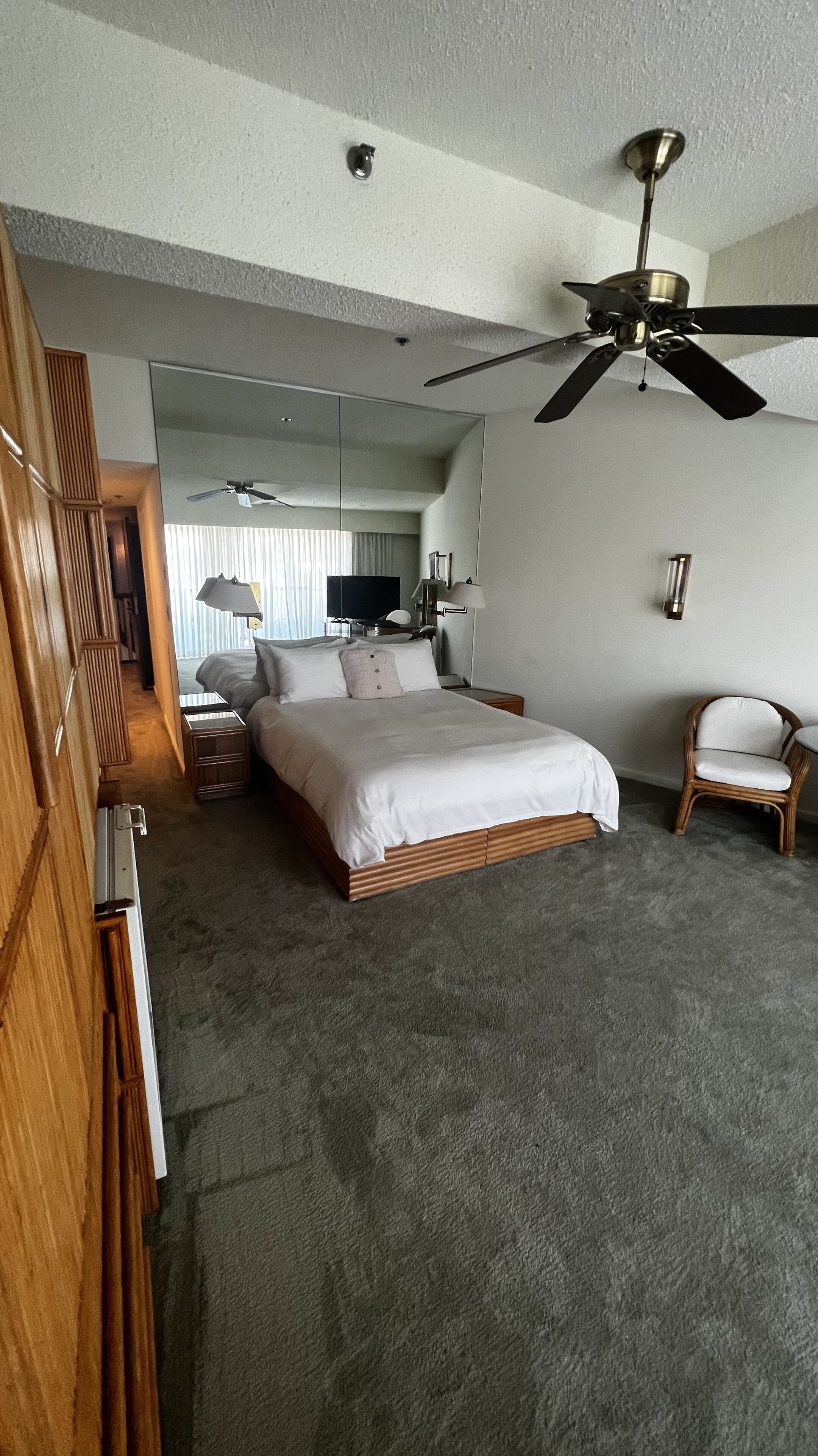 Una habitación de hotel con una cama grande, un ventilador de techo, una silla y un espejo.