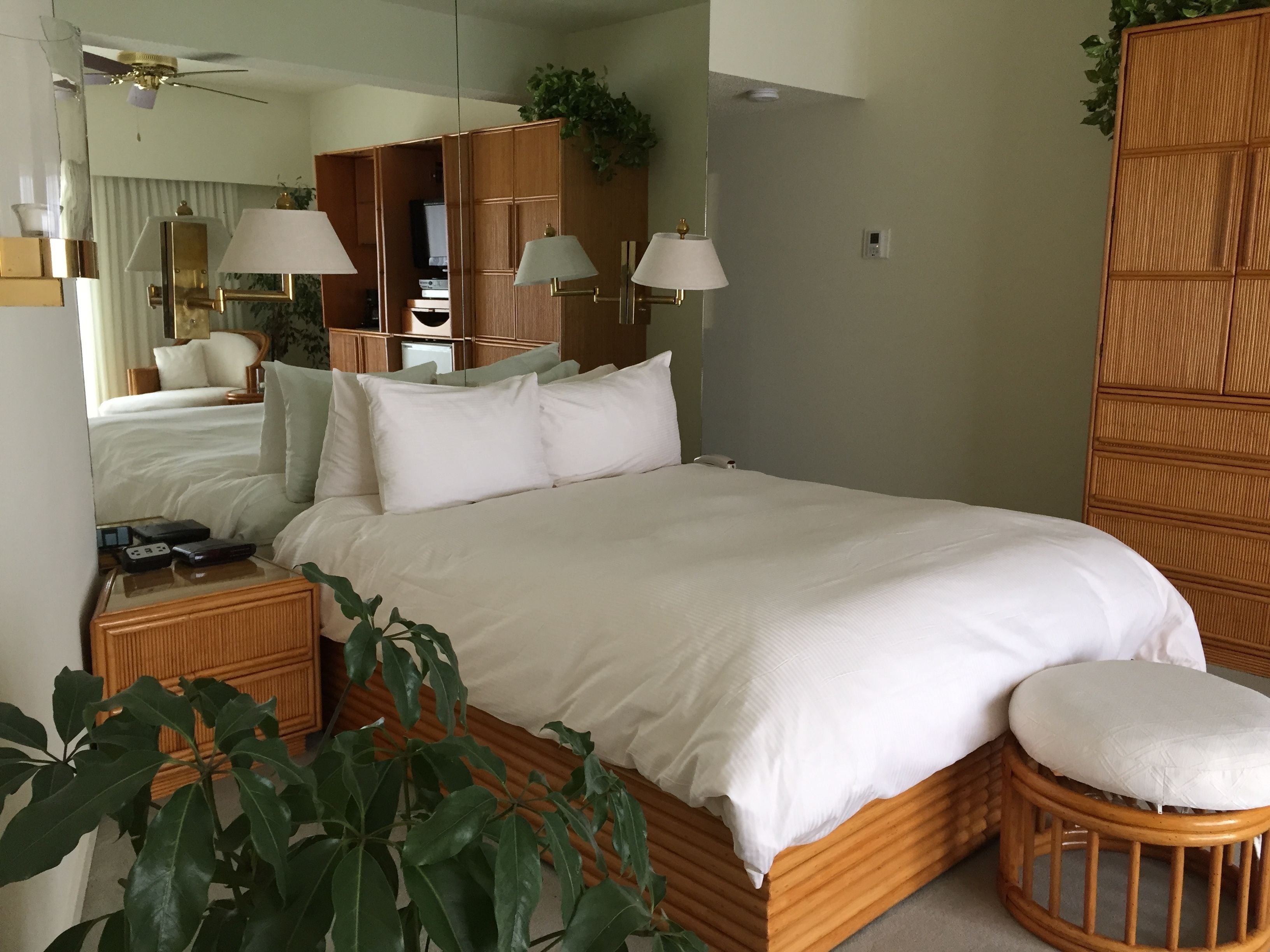 A neatly made bed with white linens, a wooden headboard, a bedside table with a lamp, and a small wooden stool.