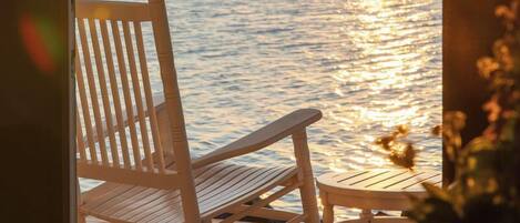 A rocking chair on a wooden deck with a view of the ocean and a sunset.