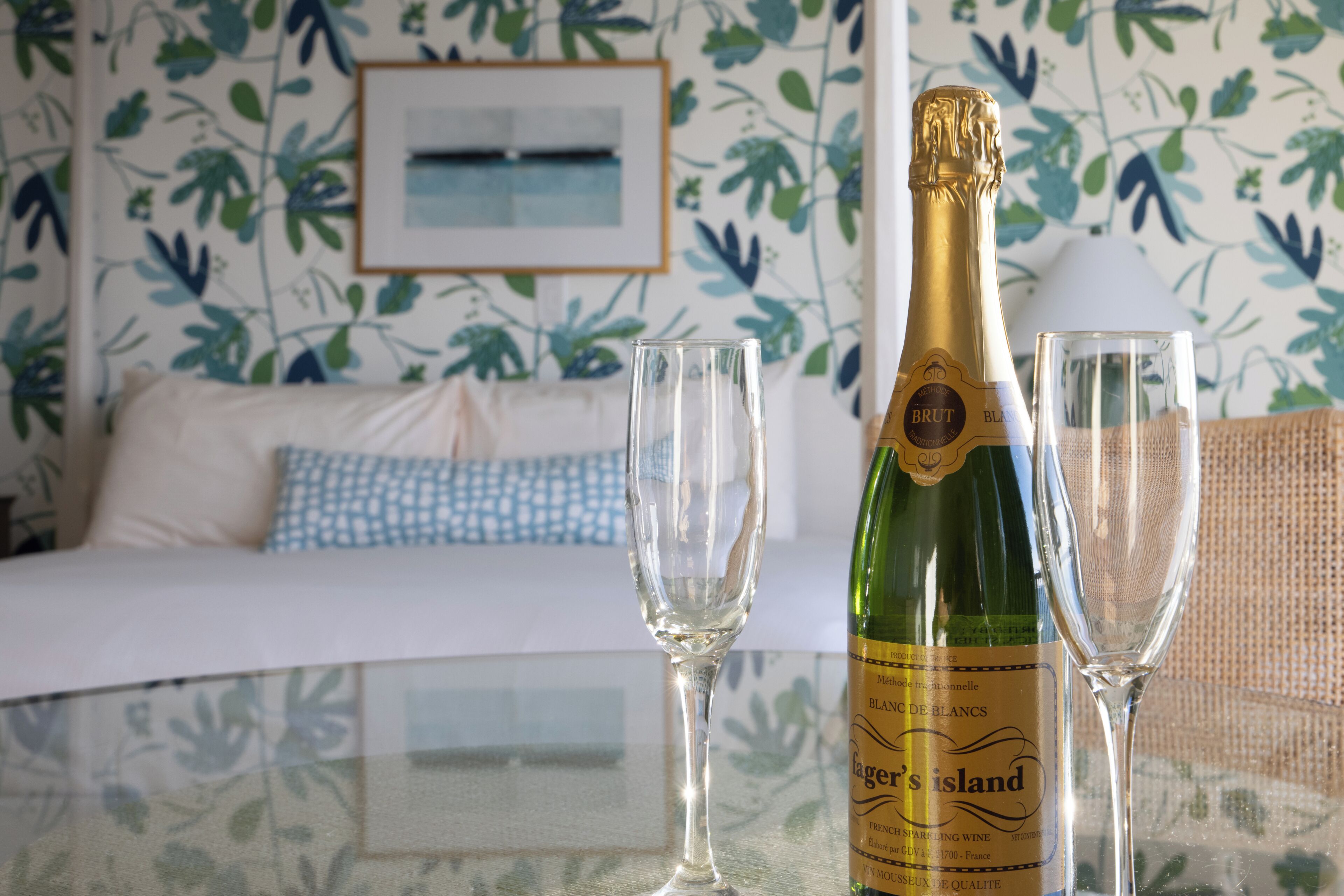 A room with a bed, a table with a bottle of Brut Blanc de Blancs champagne, and two glasses.