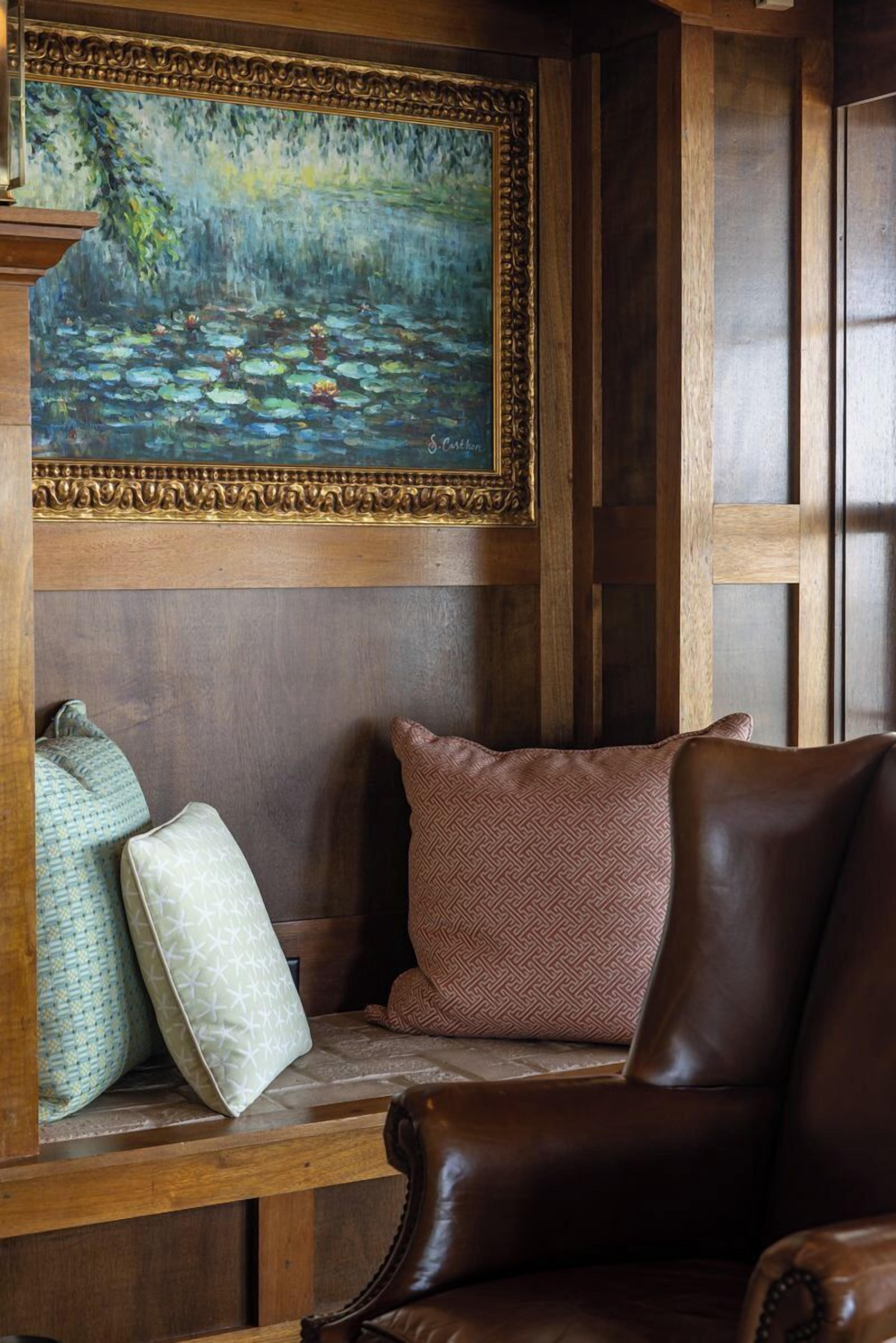 A wooden bench with cushions, a framed painting of a pond, and a wooden wall panel.