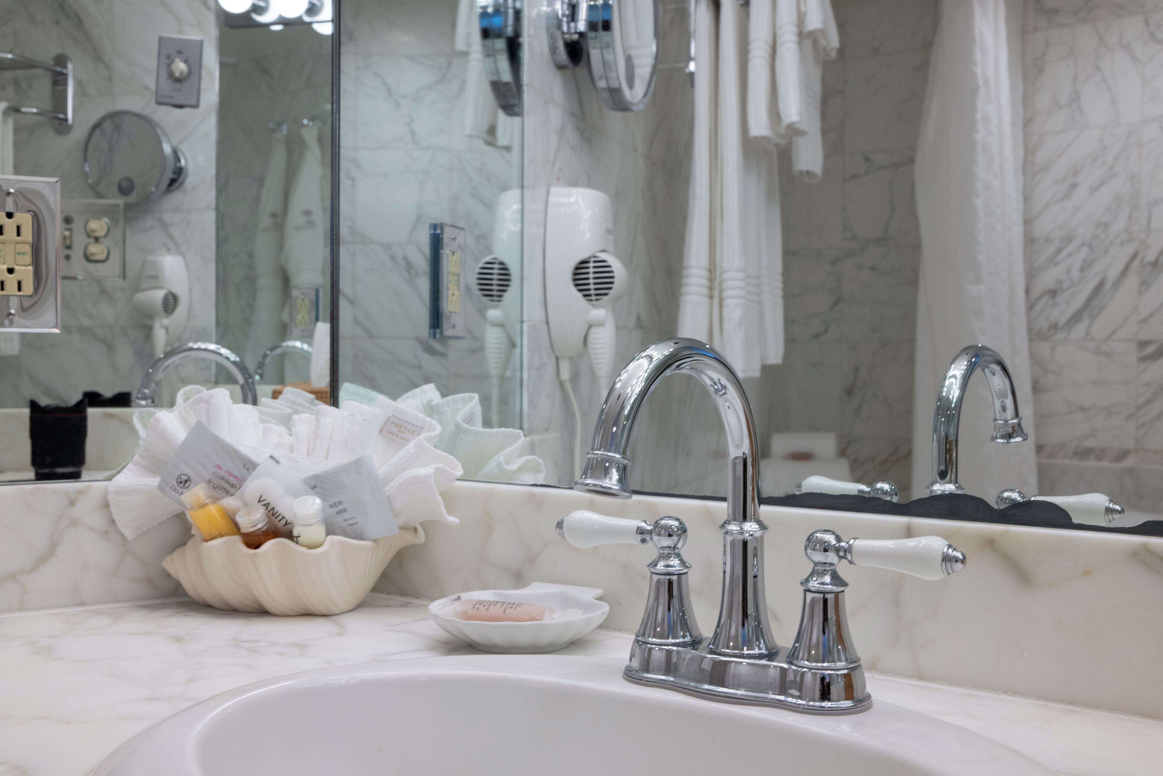 Un baño con un lavabo de mármol, dos grifos cromados, un espejo y un secador de pelo en la pared.