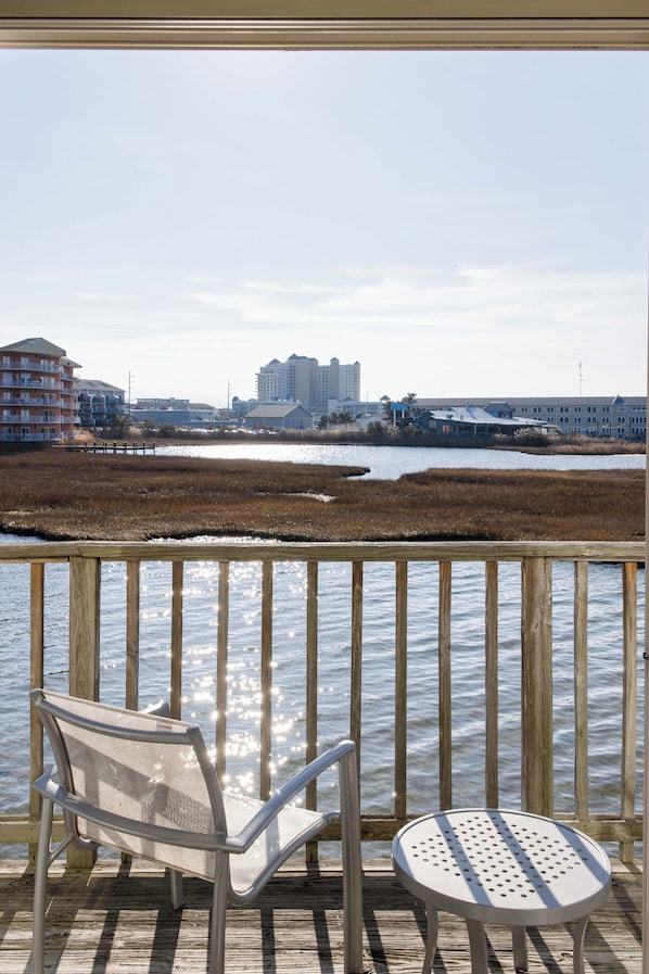 A wooden deck with a metal chair and a small table, overlooking a body of water with a distant shoreline.