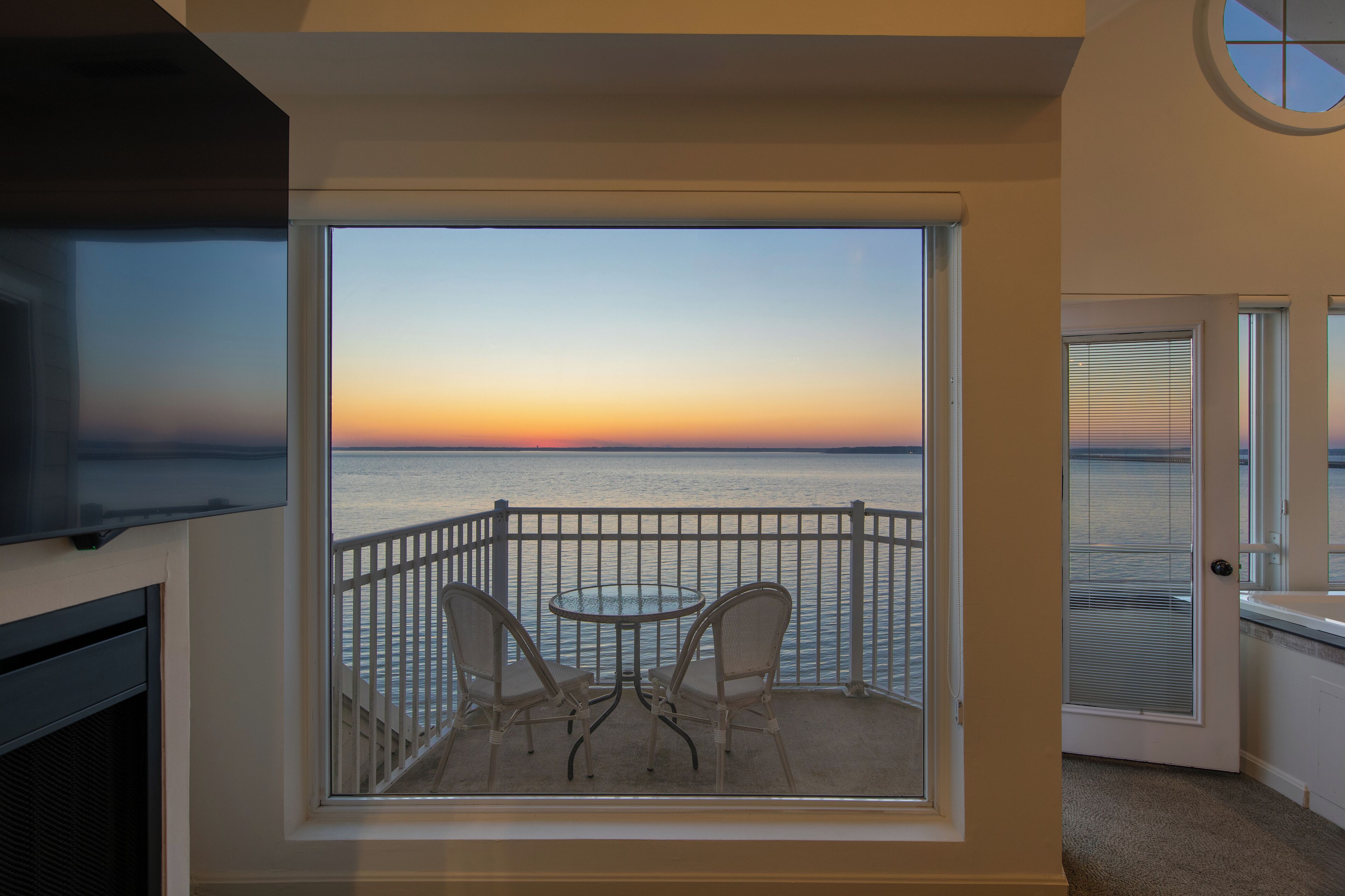 Ein Balkon mit Meerblick bei Sonnenuntergang, ein runder Tisch und zwei Stühle.